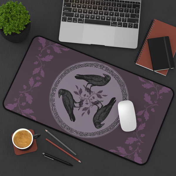 a purple mouse pad with a design of three black birds, a laptop, a keyboard, a mouse, a coffee cup, and some stationery items on a desk.