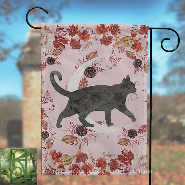 A black cat silhouette is depicted against a pink background with autumn leaves and pine cones.